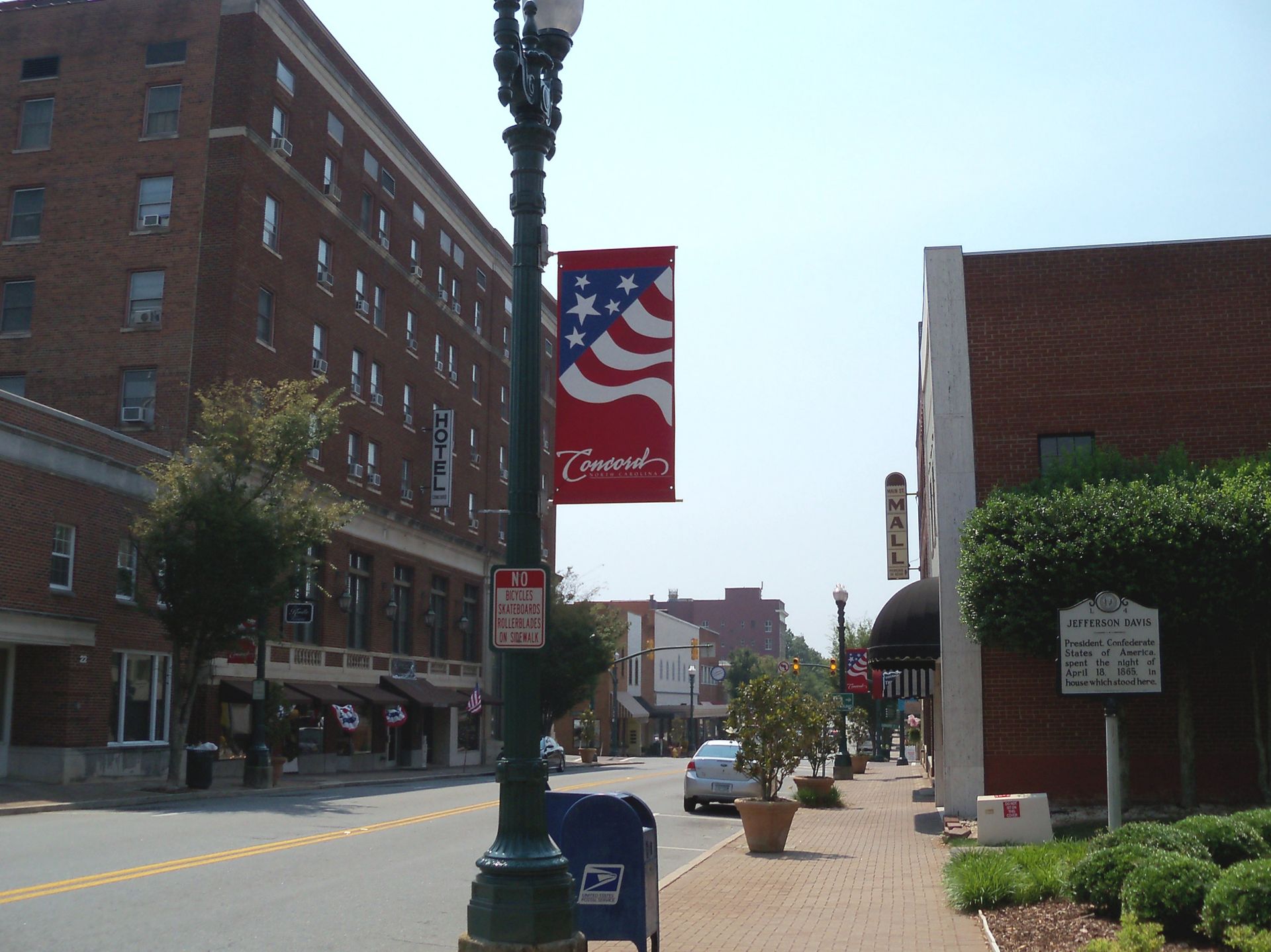 Street scene in Thomasville, NC, with banner of American flag design, brick buildings, and parked cars.