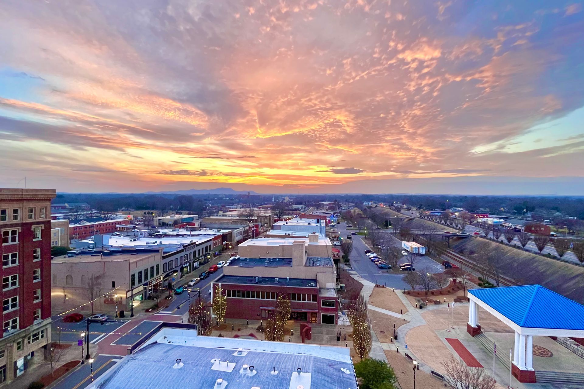 Sunset over downtown area, buildings, streets, and park, with orange and blue sky.