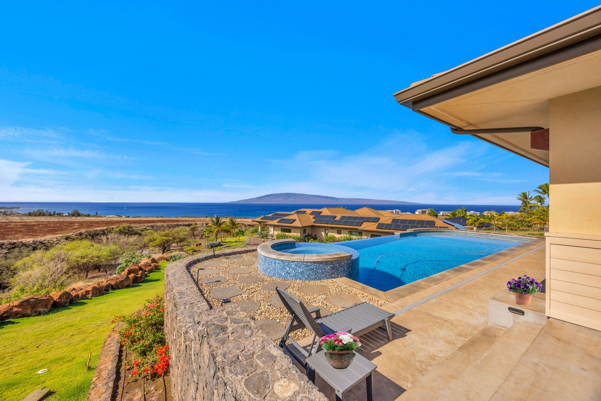 A patio with a pool and hot tub overlooking the ocean and a distant island under a clear blue sky.