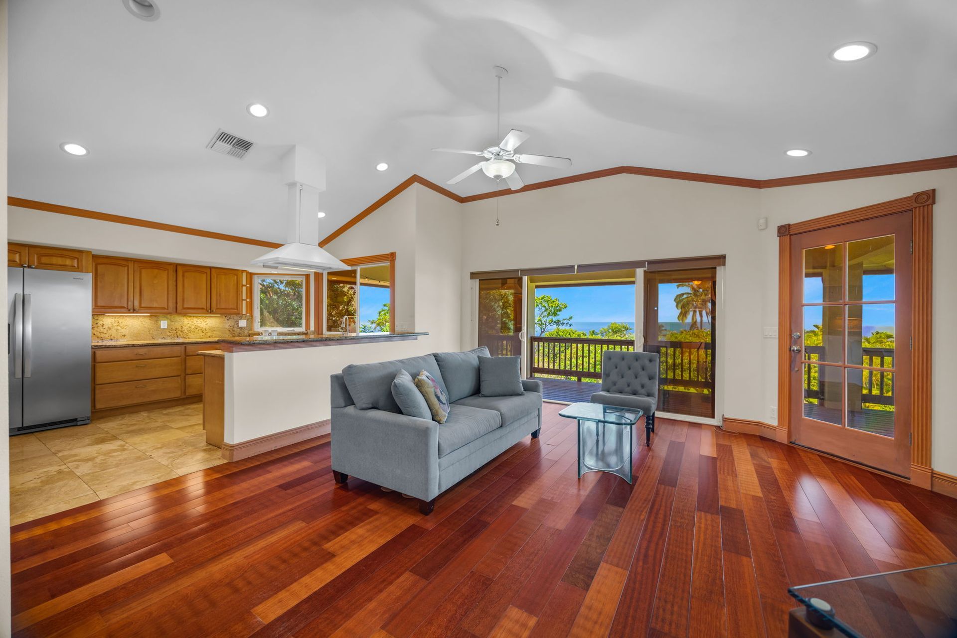 Open-plan living room with wood floors, blue sofa, kitchen, and glass doors leading to a balcony with ocean view.