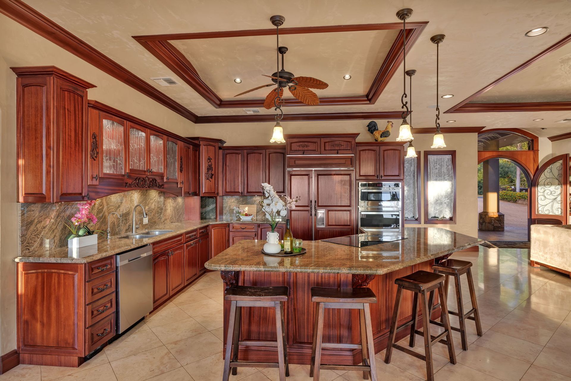 A kitchen with dark wood cabinetry, a granite-topped island with stools, and a ceiling fan in a recessed tray ceiling.