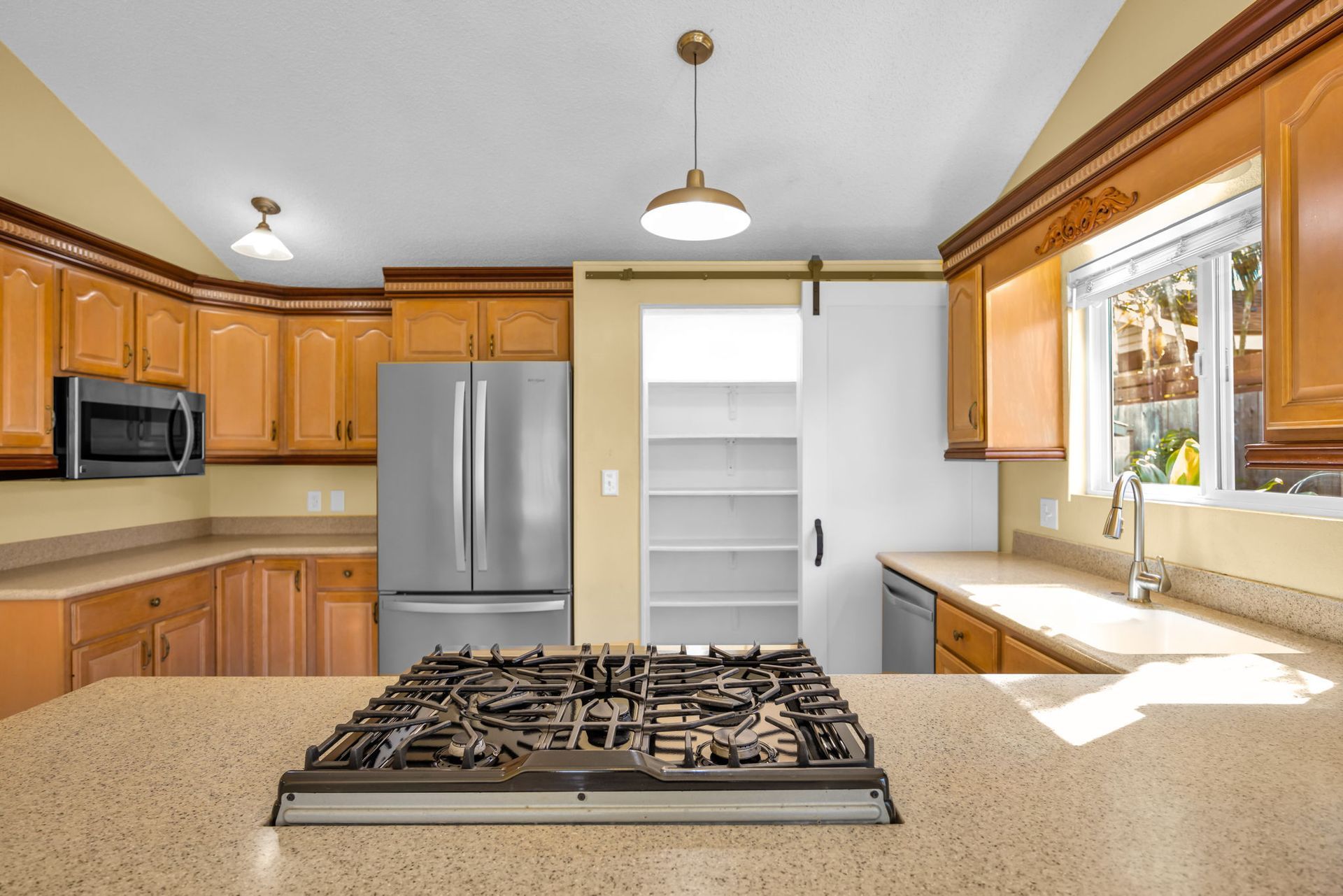 A kitchen with wood cabinets, stainless steel appliances, a center island with a gas cooktop, and a white sliding door.