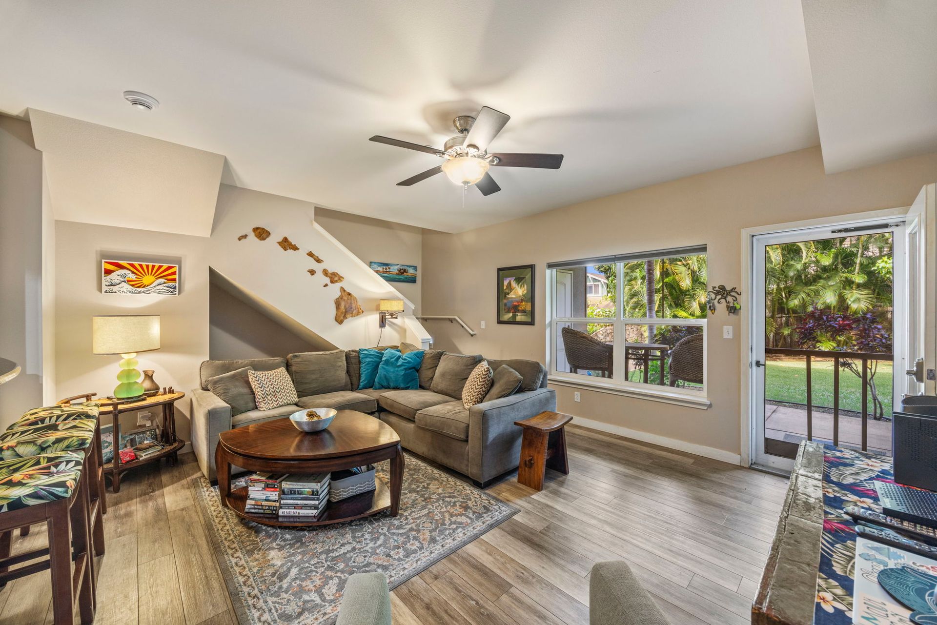 A cozy living room with a gray sectional, wooden coffee table, wall art of Hawaii, and a door opening to a patio.