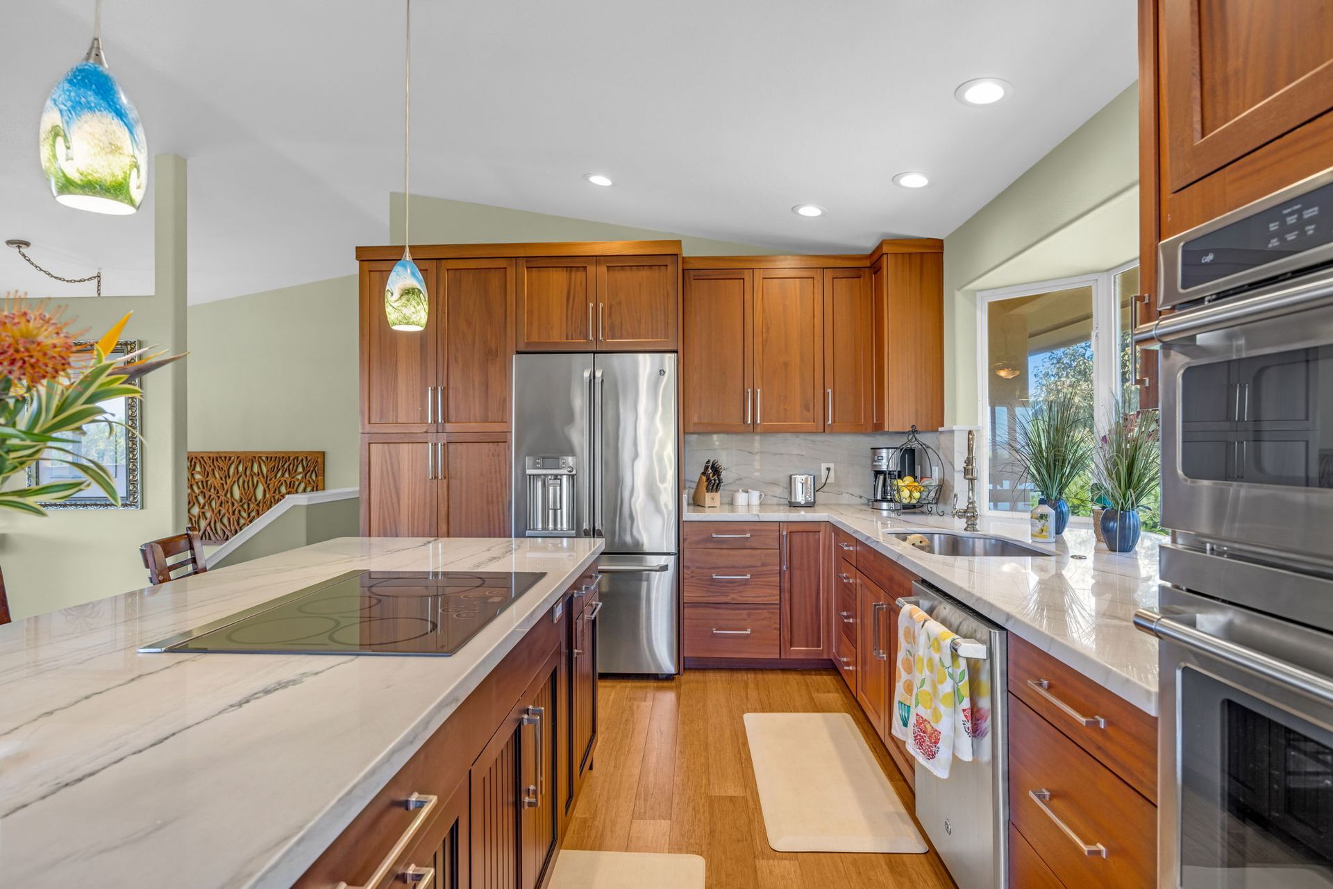 Modern kitchen with wood cabinets, stainless steel appliances, a large marble island, and colorful pendant lights.
