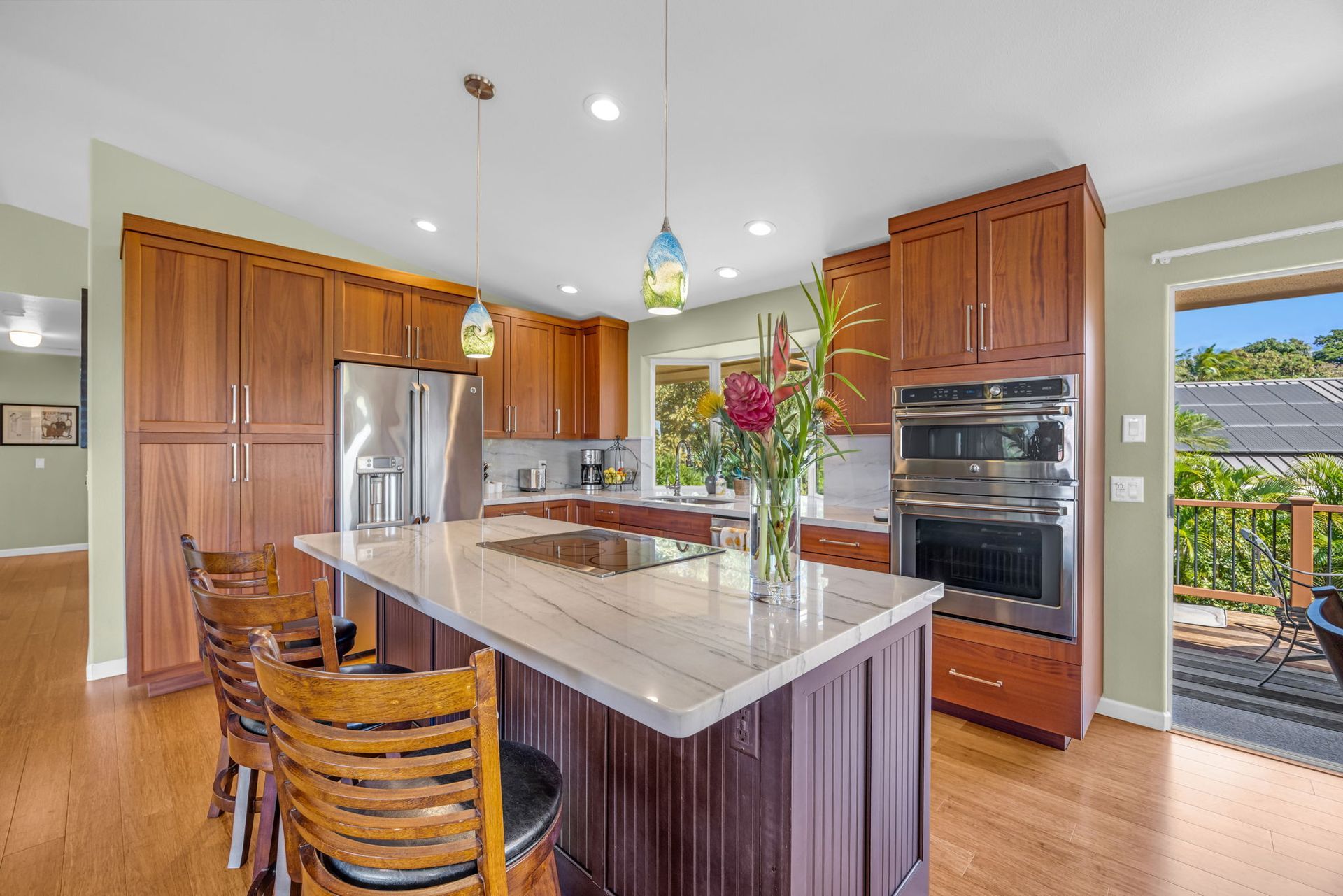 A kitchen with medium-wood cabinets, a large stone-topped island with seating, a stainless refrigerator, and an oven.