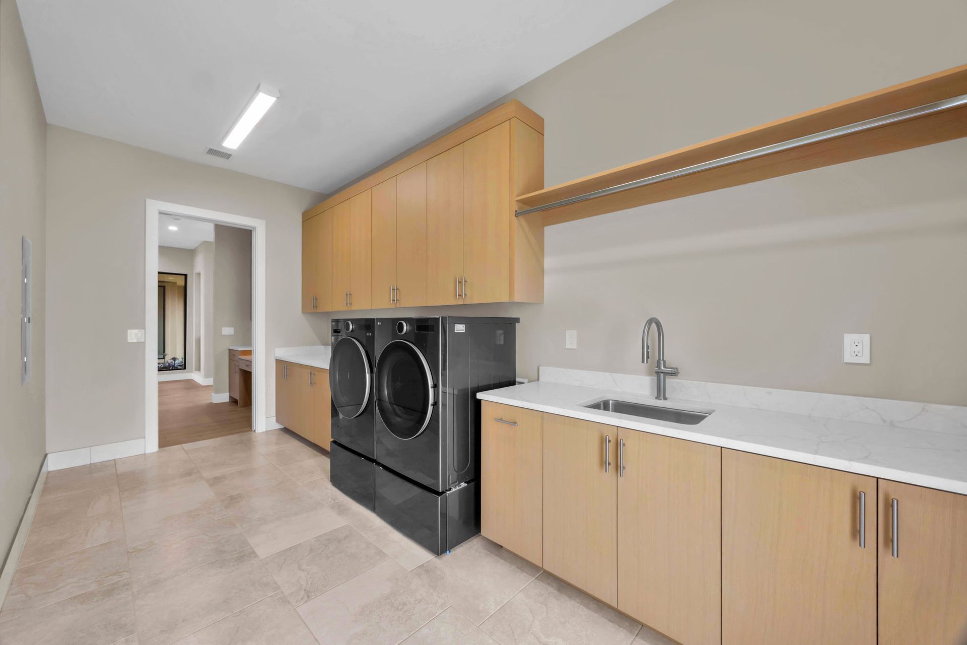 A laundry room featuring light wood cabinets, dark appliances, a white countertop, and a stainless steel sink.