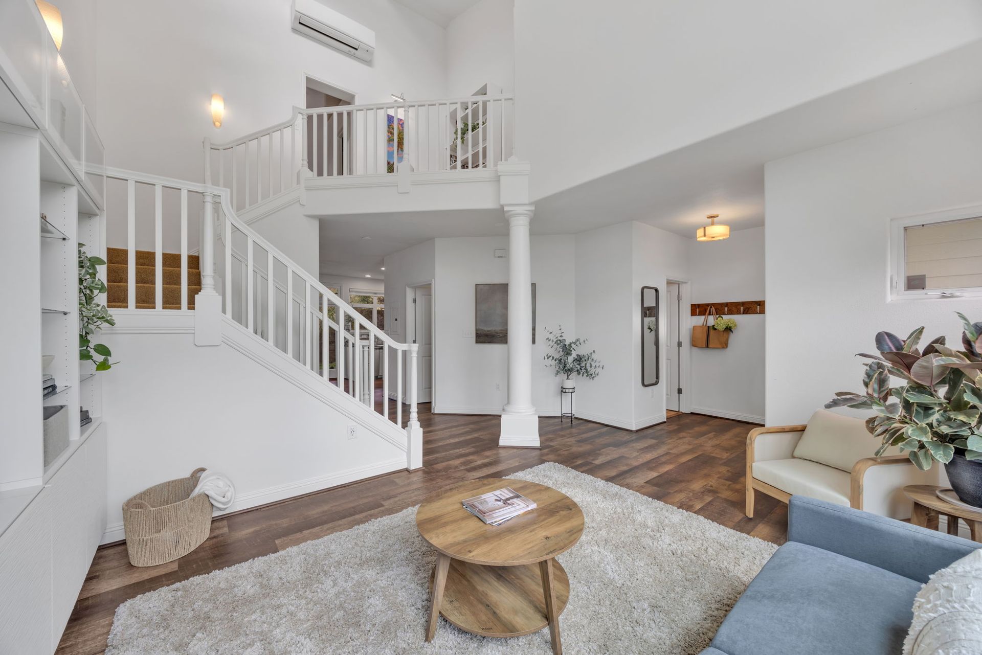 A modern living room with wood floors, a shaggy area rug, a round coffee table, staircase, and a light-colored armchair.