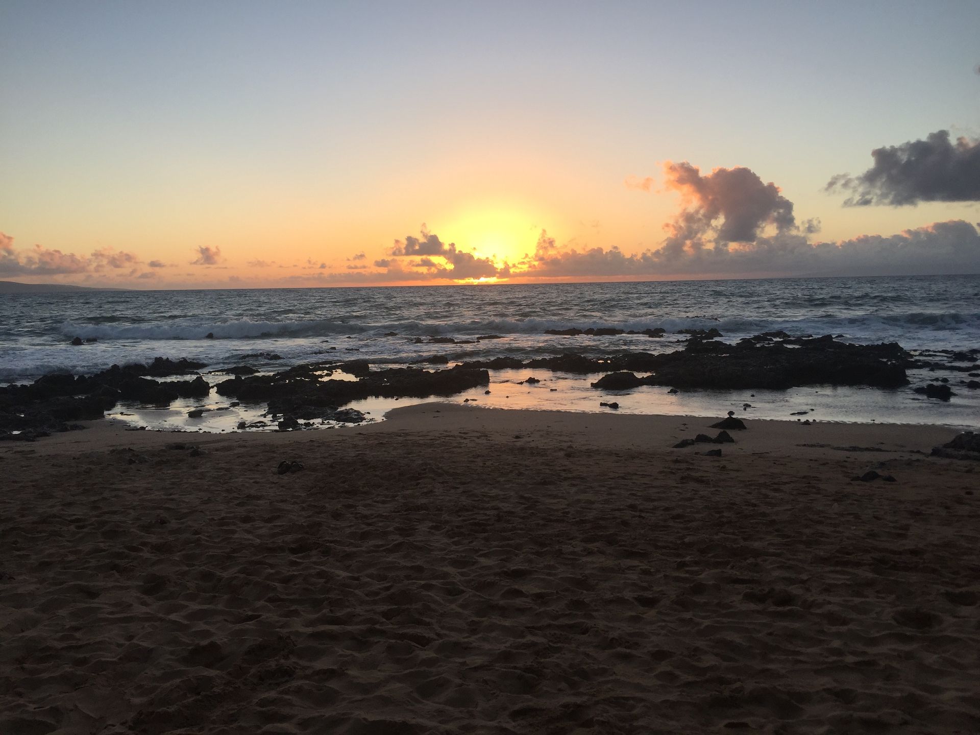 A scenic sunset over a rocky coastline with golden light reflecting on the ocean waves and sandy shore.