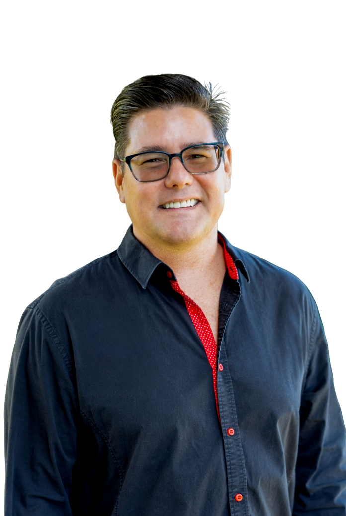 A smiling person with dark hair and glasses, wearing a black button-down shirt with red trim, against a white background.