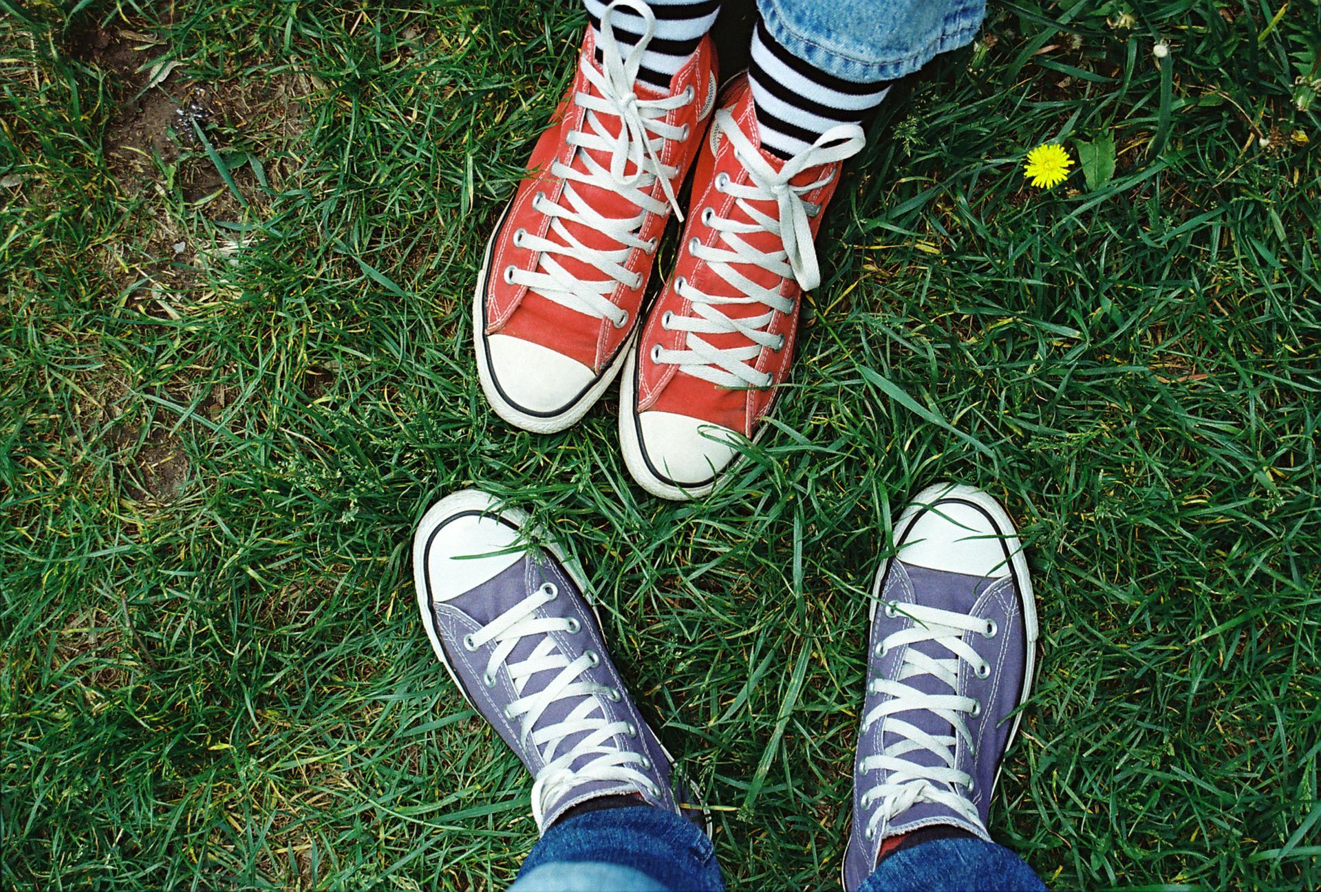 Two pairs of canvas sneakers, one red and one blue, stand on green grass.