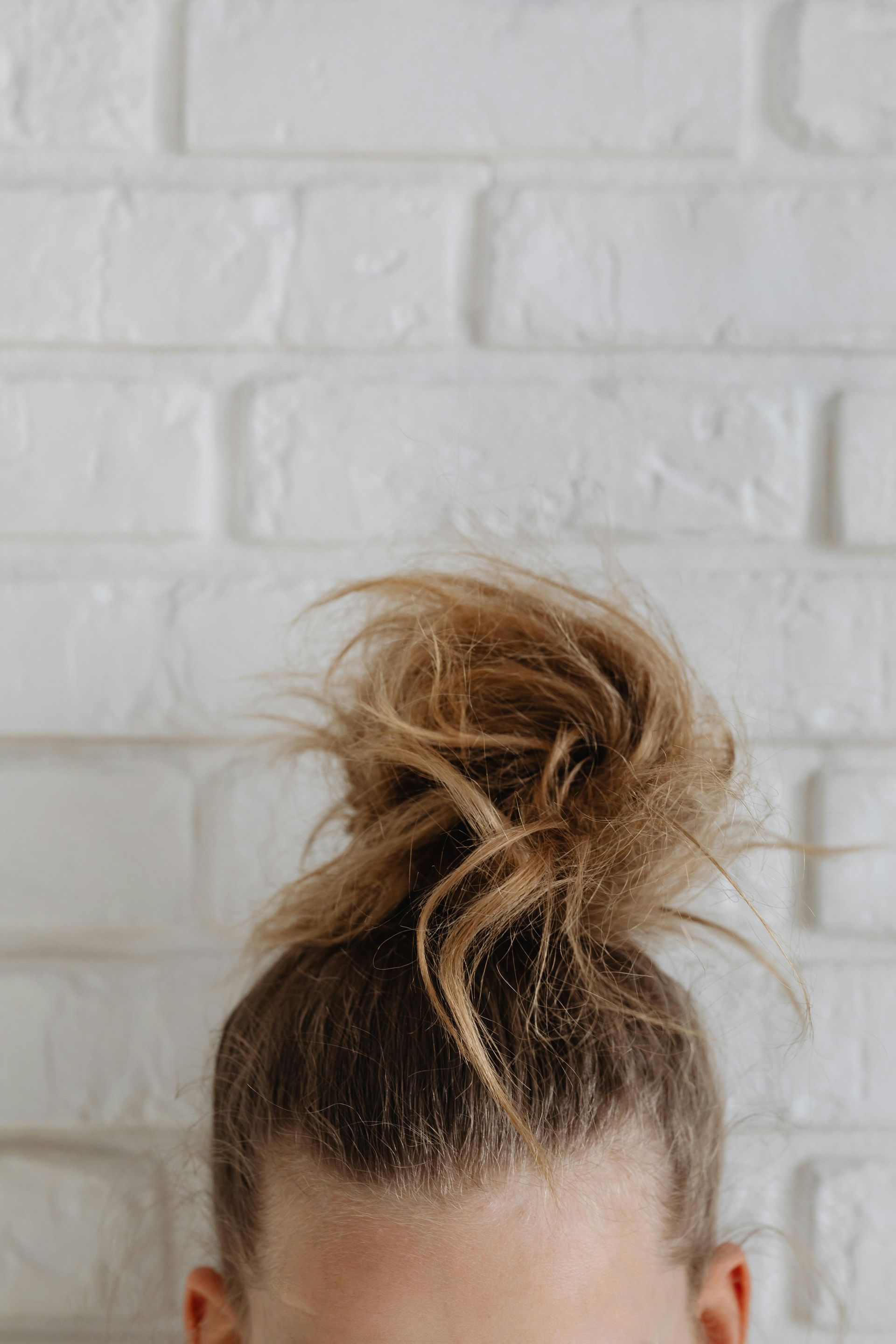 A messy, light brown bun hairstyle set against a white, textured brick wall.