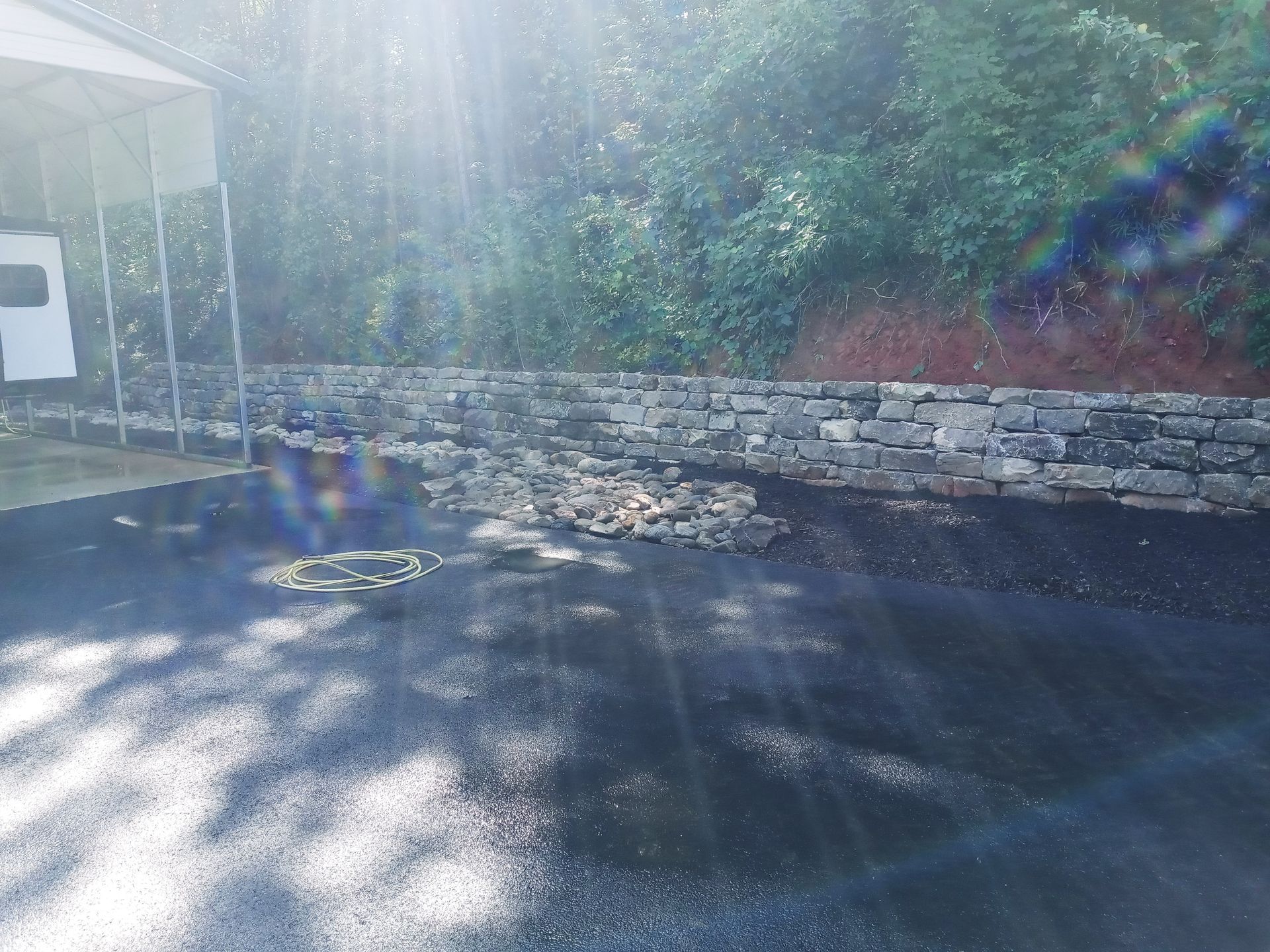 A driveway with a stone wall and a carport in the background.