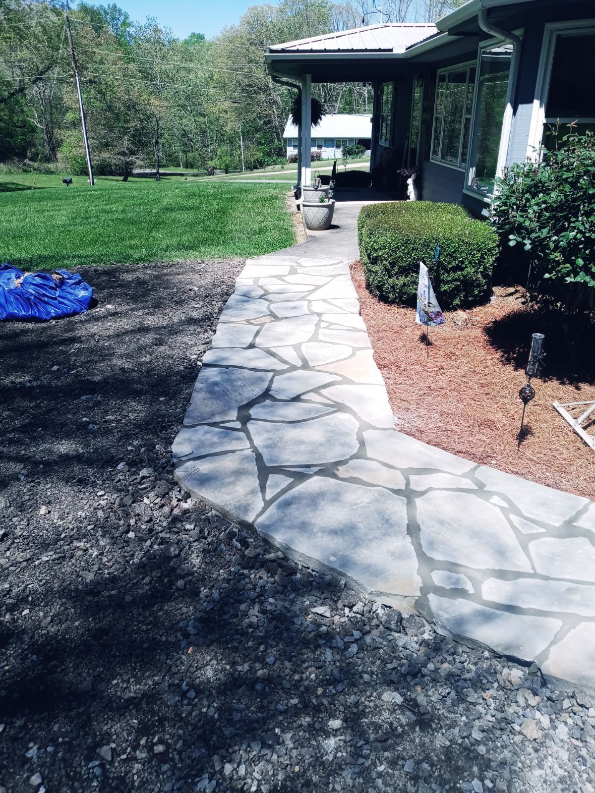 A stone walkway leading to a house with a blue tarp on the ground.