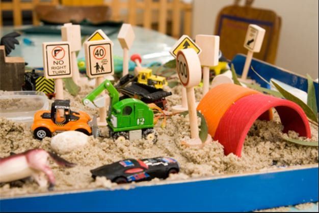 A box filled with sand and toy cars and signs.