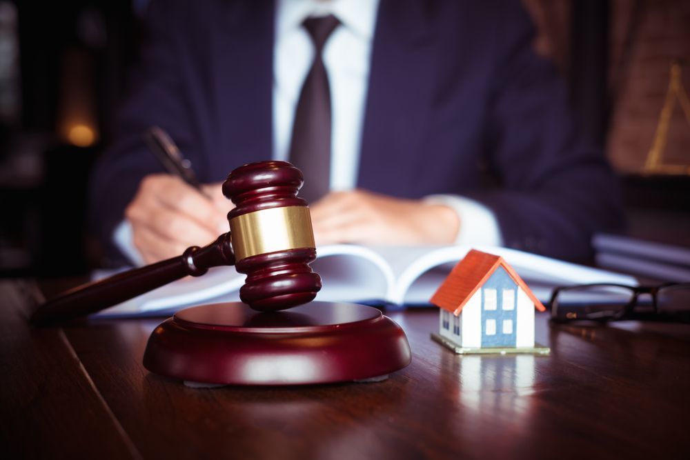 A Man is Sitting at a Table With a Gavel and a Small House — ACT Law Associates In Woden, ACT