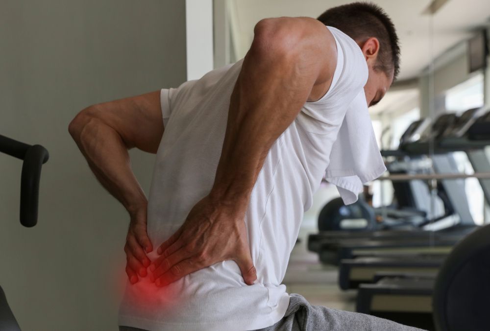 A man is holding his sore back at the gym — ACT Law Associates In Canberra, ACT