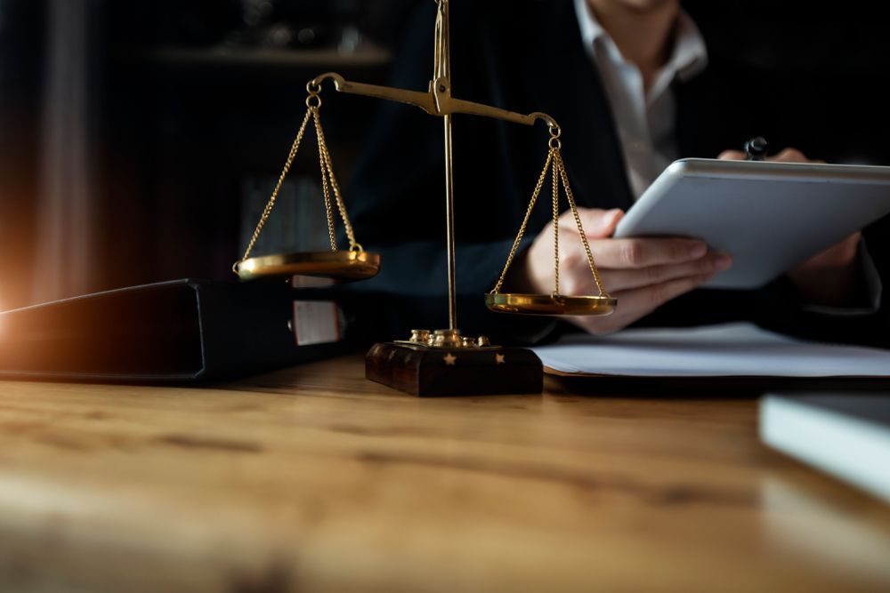 A Woman is Sitting at a Table With a Scale of Justice and a Tablet — ACT Law Associates In Fyshwick, ACT