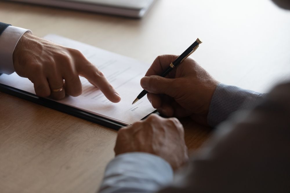A Man is Signing a Document While Another Man Points at It — ACT Law Associates In Canberra, ACT