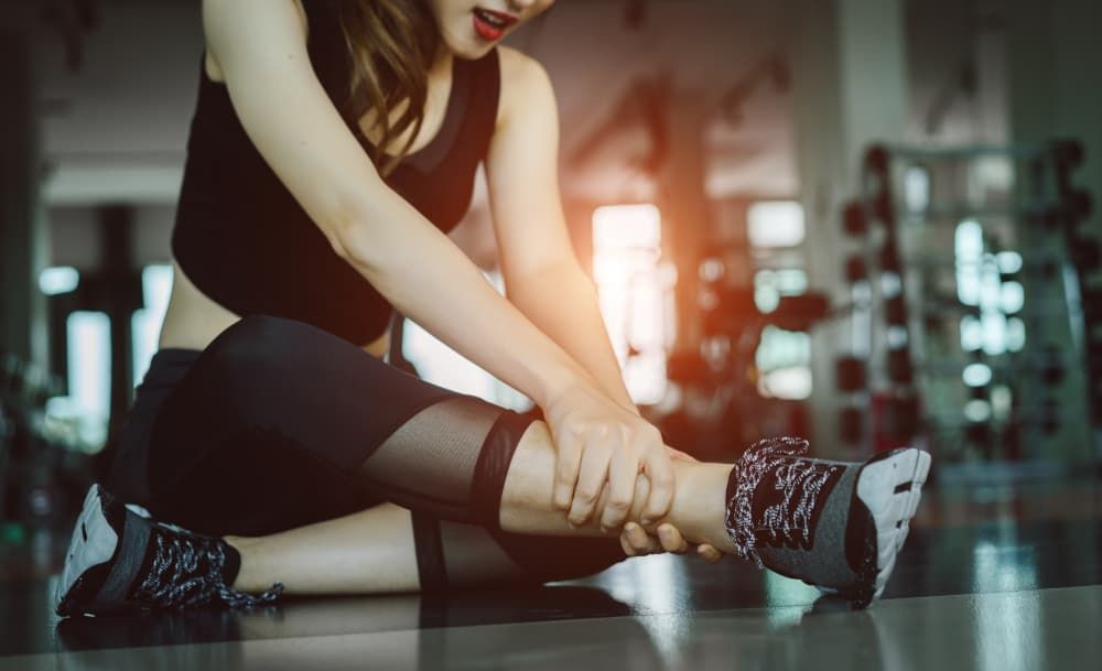 A Woman is Sitting on the Floor in a Gym Holding Her Ankle in Pain — ACT Law Associates In Canberra, ACT