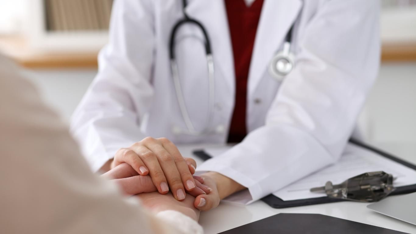 A Doctor is Holding a Patient's Hand While Sitting at a Desk — ACT Law Associates In Gungahlin, ACT