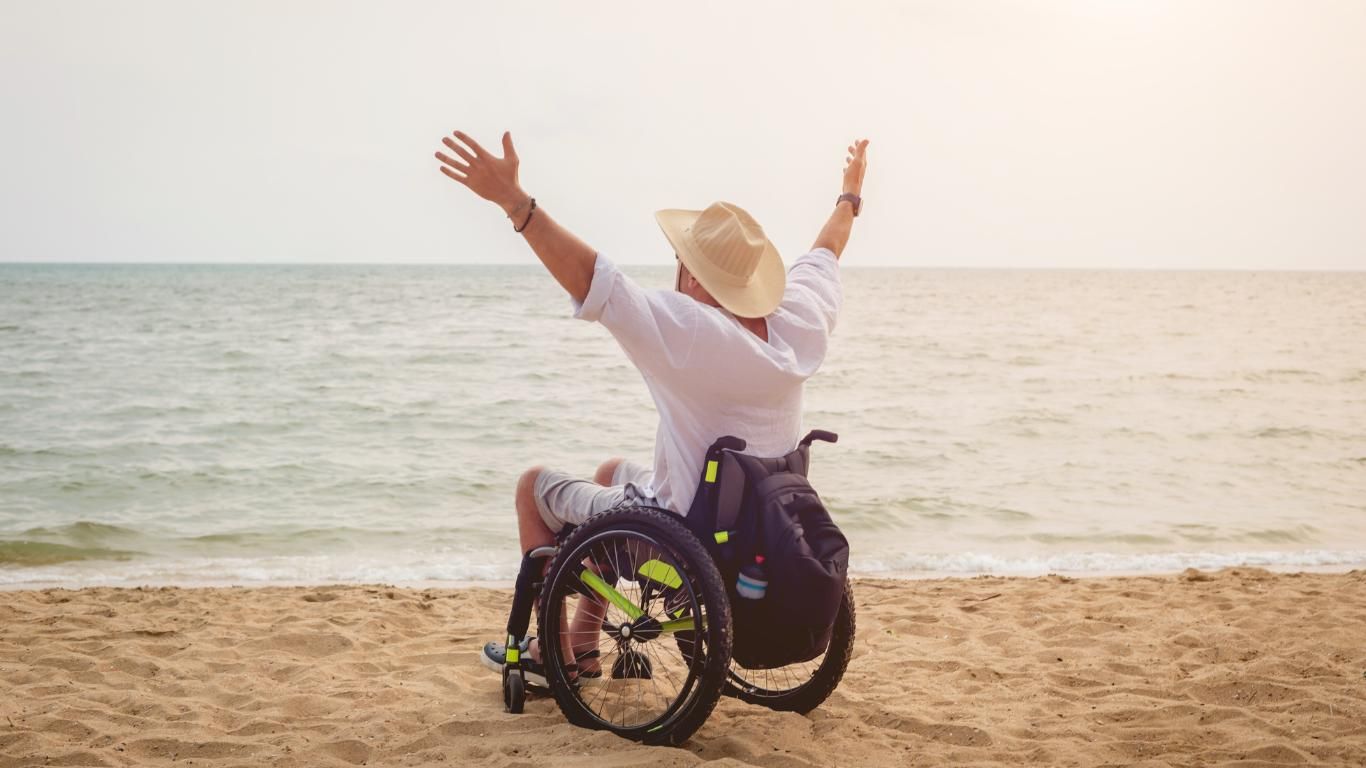A Man in a Wheelchair is Sitting on the Beach With His Arms Outstretched — ACT Law Associates In Gungahlin, ACT