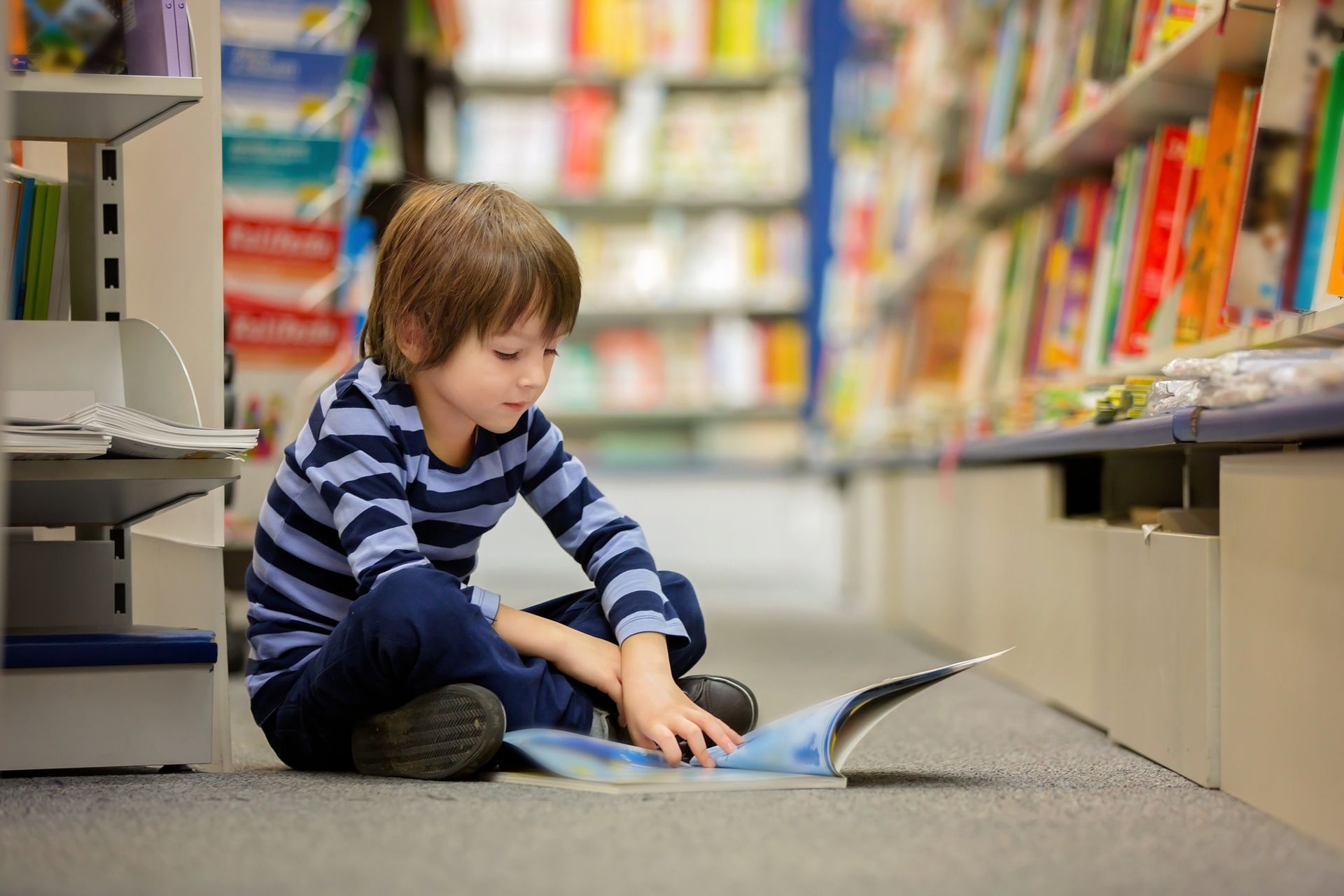 Boy reading a book as he sits on the floor at a library