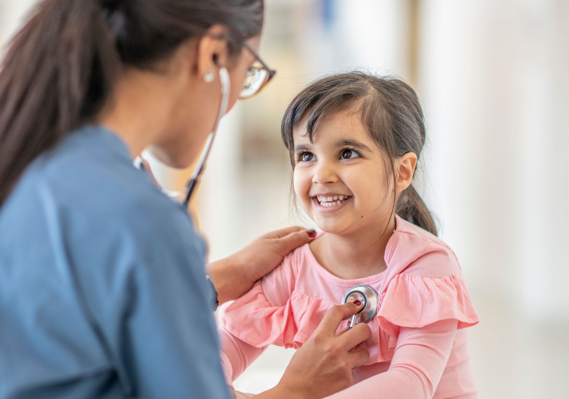 A nurse is listening to a little girl 's heart with a stethoscope.