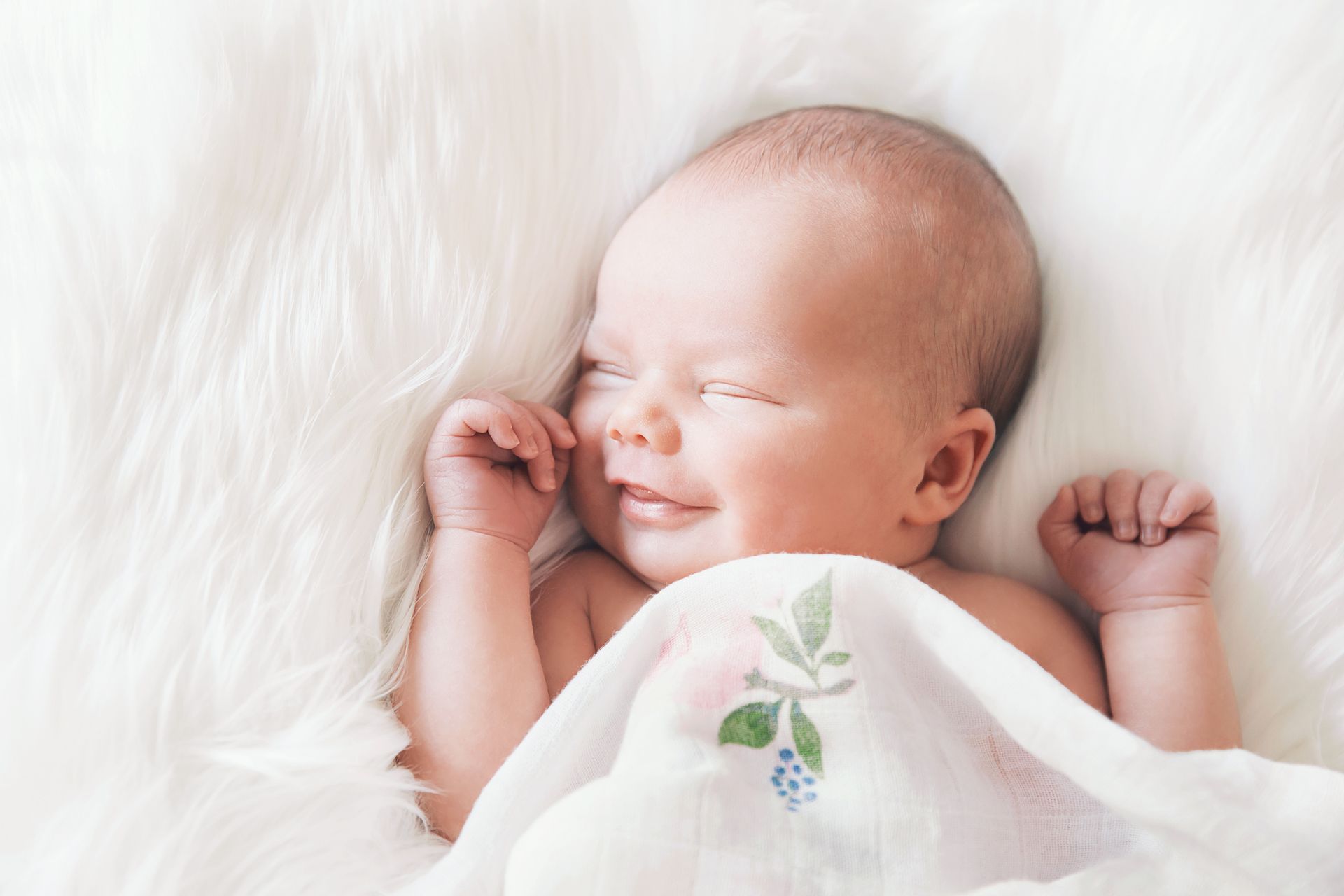 Smiling newborn baby snuggled up in white blankets
