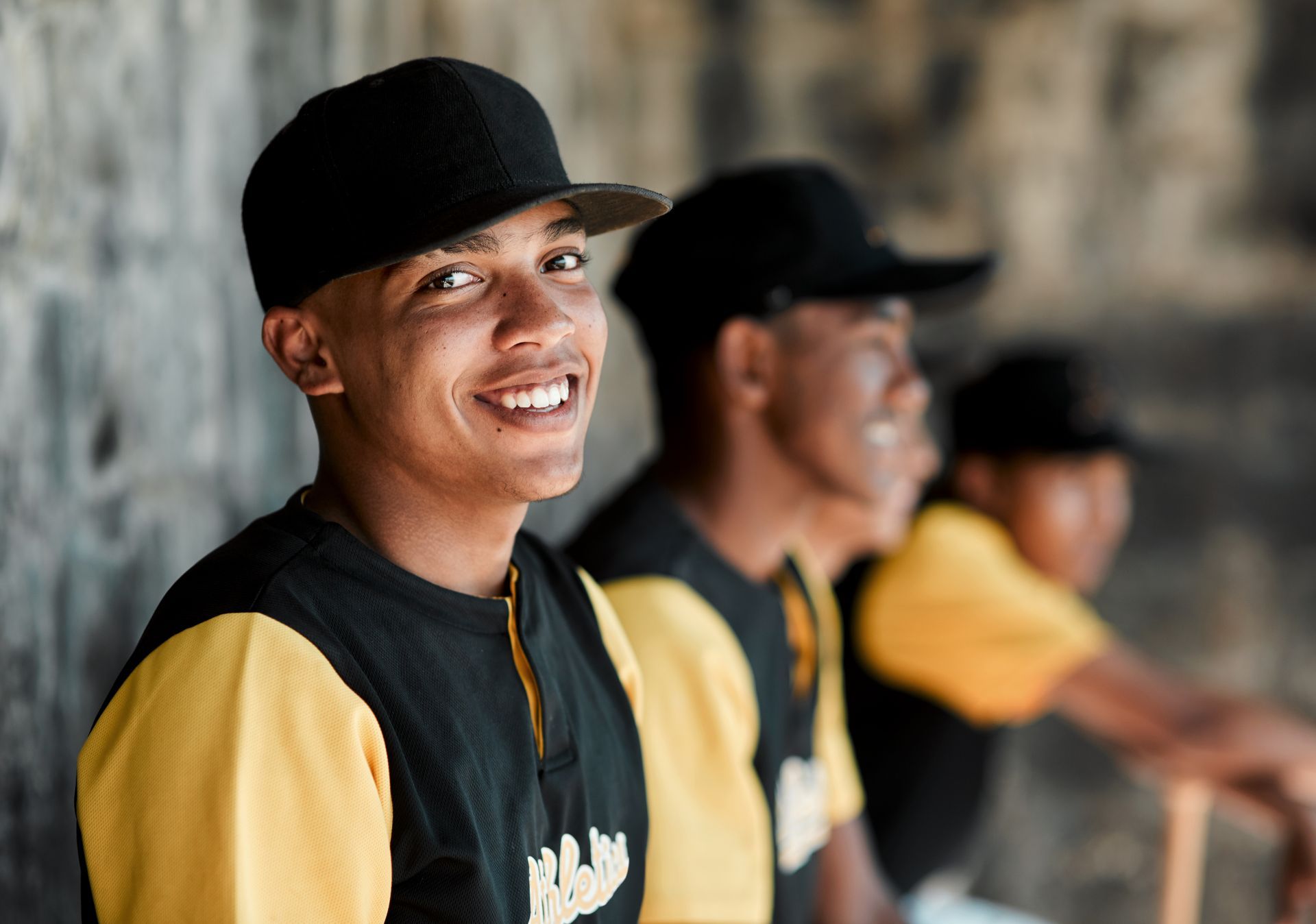 Smiling baseball player sitting in the dugout with team members