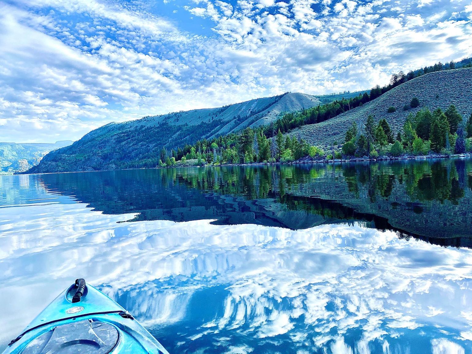 Kayaking on a calm blue lake with forested mountains and a mirrored sky reflection