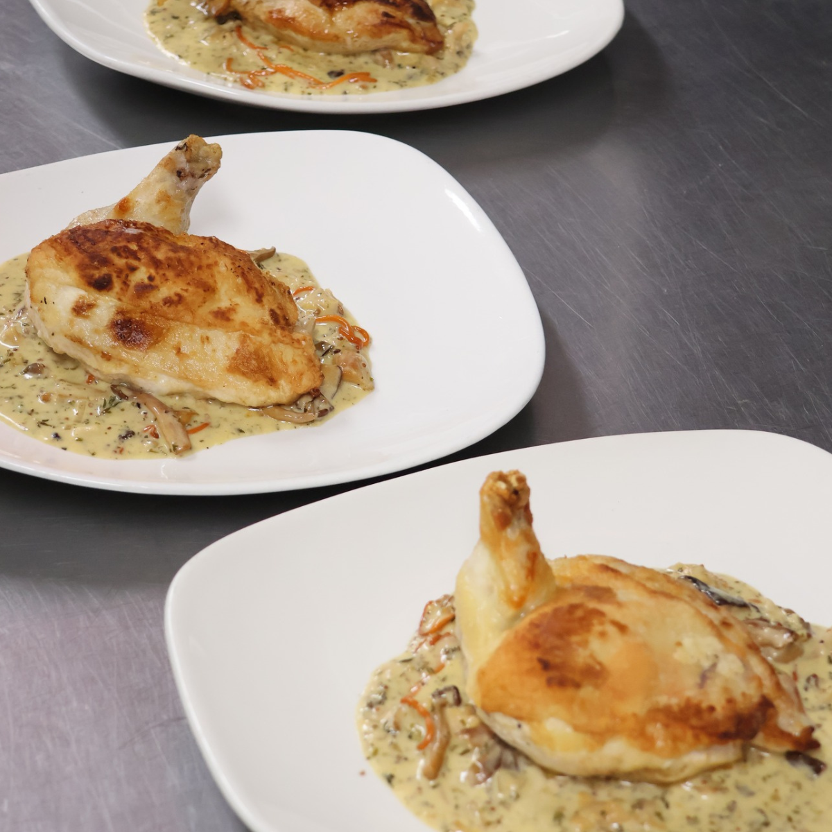 Plated roasted chicken pieces on a creamy sauce, arranged on a stainless-steel counter