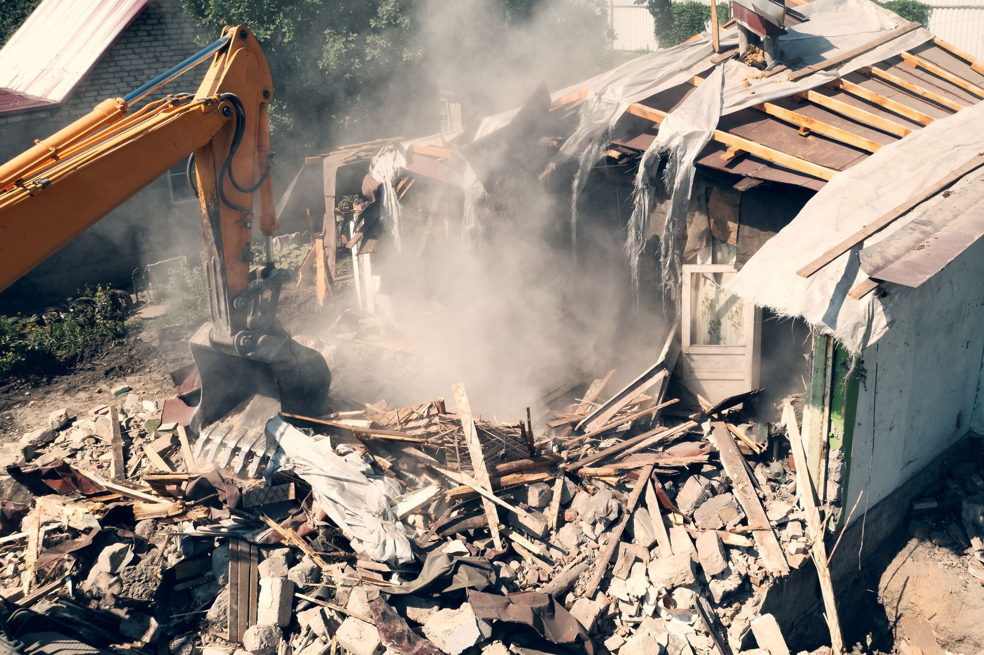 A yellow excavator is demolishing a house with smoke coming out of it.