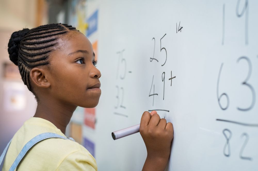 Black girl, approximately age 10, at blackboard doing mathematical equations.