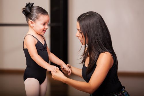 White mother with long hair kneeling in front of her four-year-old daughter, dressed as a ballerina.
