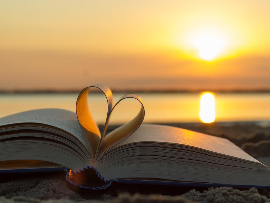 Book on beach with pages folded into a heart shape; sunset in the background.
