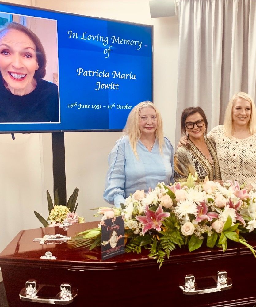 Three Women Are Standing in Front of A Coffin with Flowers