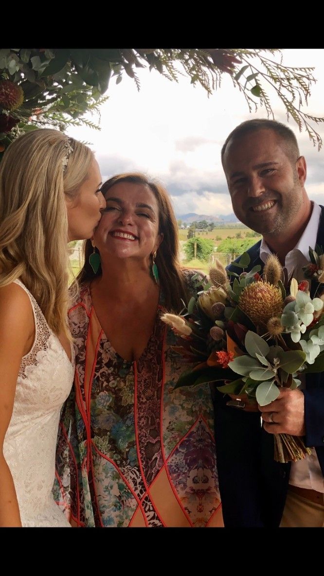 A Bride and Groom Are Posing for A Picture with A Woman Kissing the Bride on The Cheek
