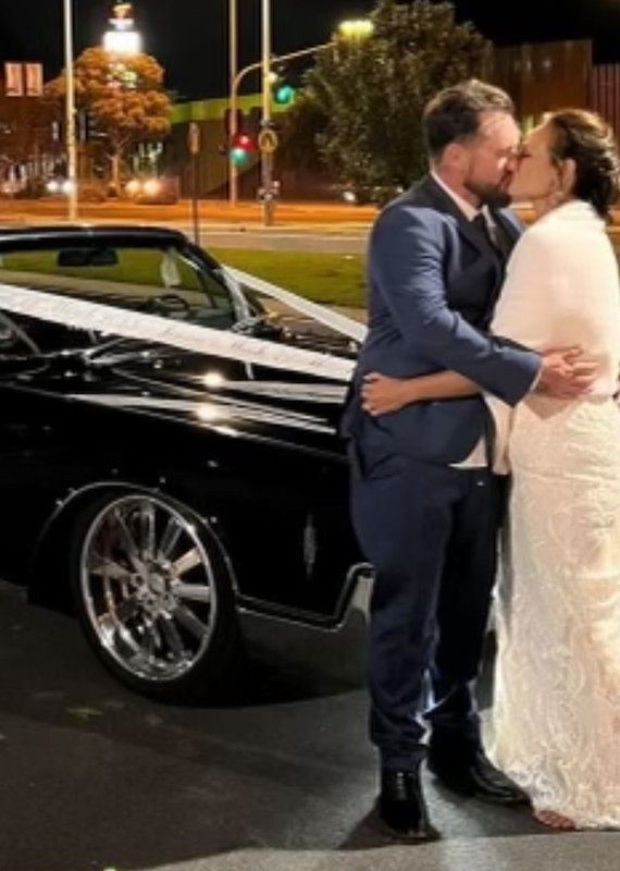 A Bride and Groom Are Kissing in Front of A Black Car