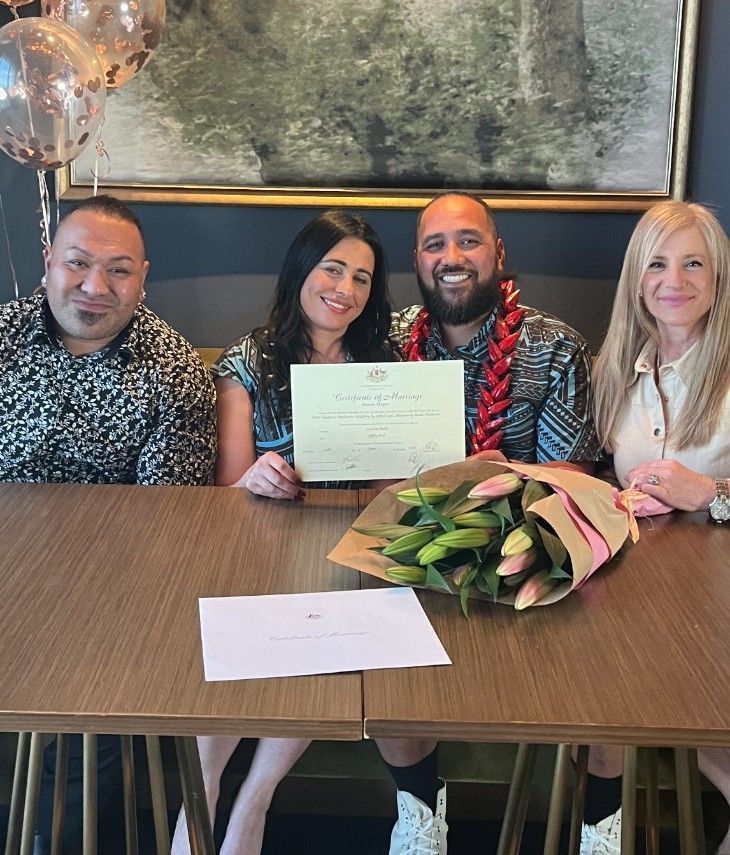 Four people are sitting at a table holding a certificate and a bouquet of flowers.