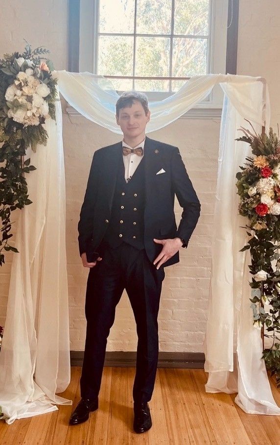 A Man in A Suit and Bow Tie Is Standing in Front of A Floral Arch