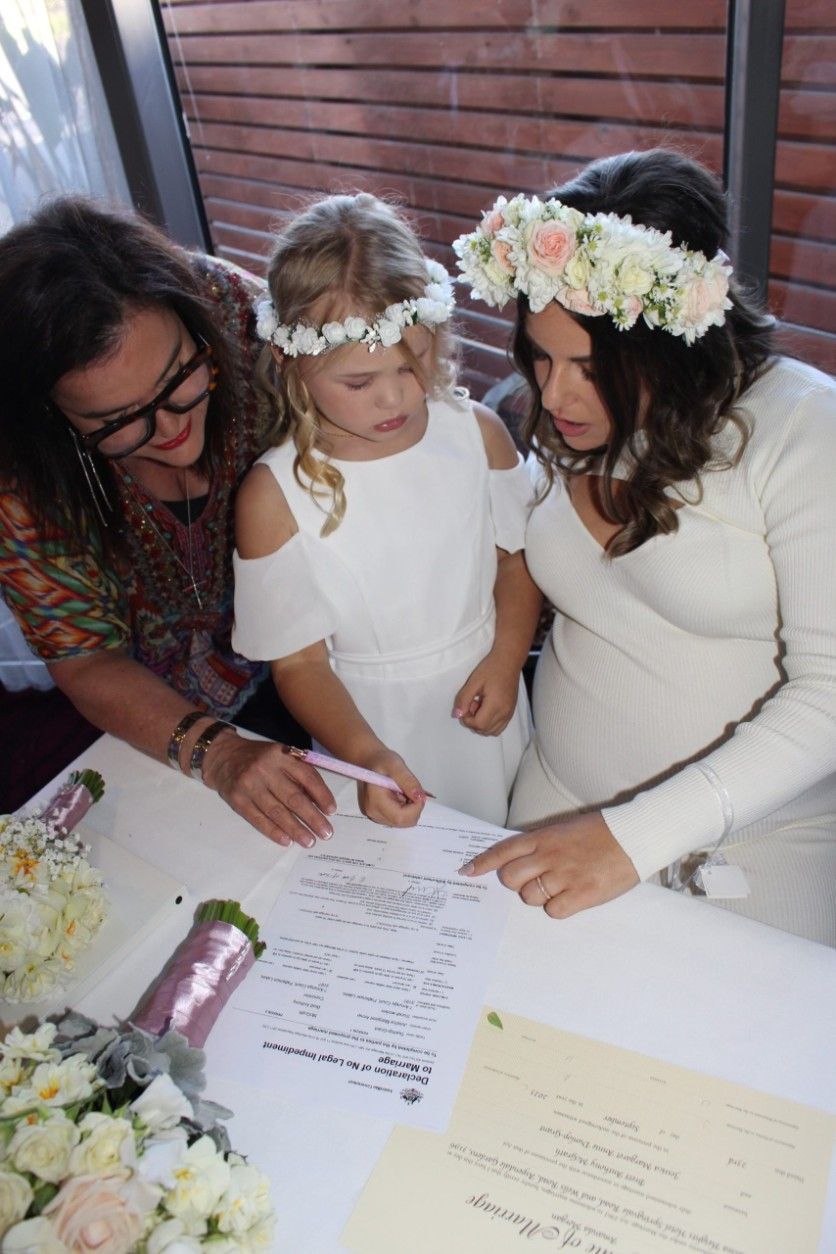 A Little Girl Wearing a Flower Crown Is Signing a Document with Two Women