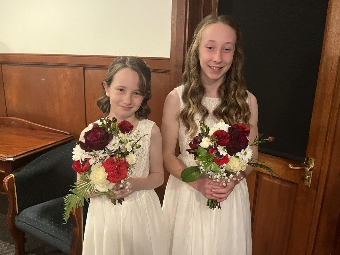Two Flower Girls in White Dresses Are Holding Bouquets of Flowers