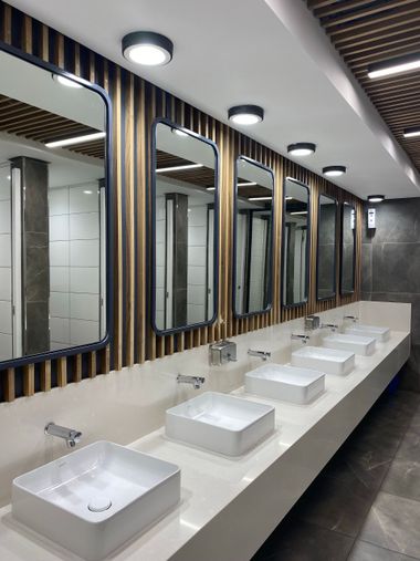 Modern restroom with row of white sinks, mirrors, and wood-accented walls
