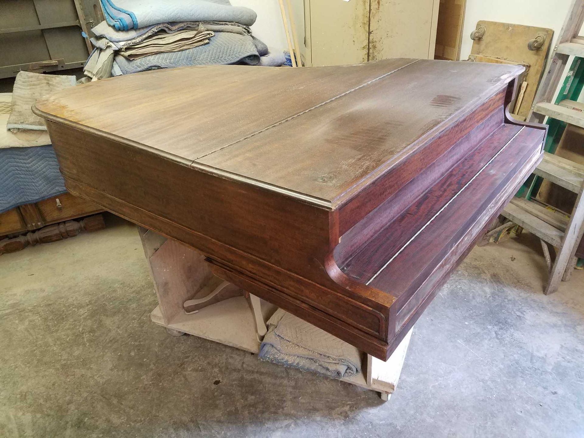 A wooden piano undergoing restoration, set in a cluttered workshop.