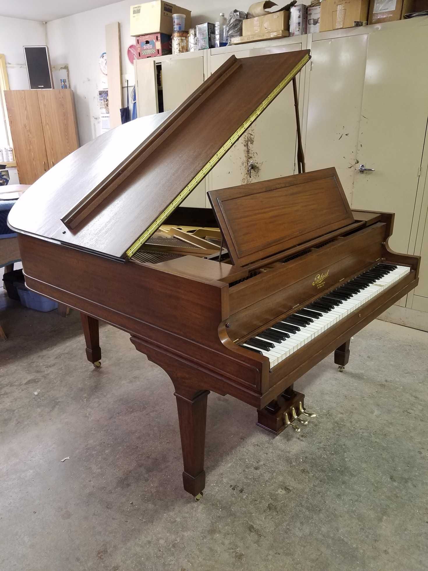 Grand piano, brown wood, open lid, white and black keys, in a room.