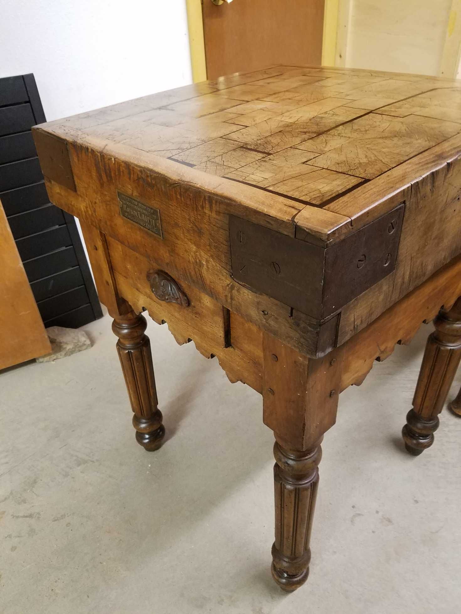 Antique wooden butcher block table with metal corner reinforcements, decorative legs, and a drawer.