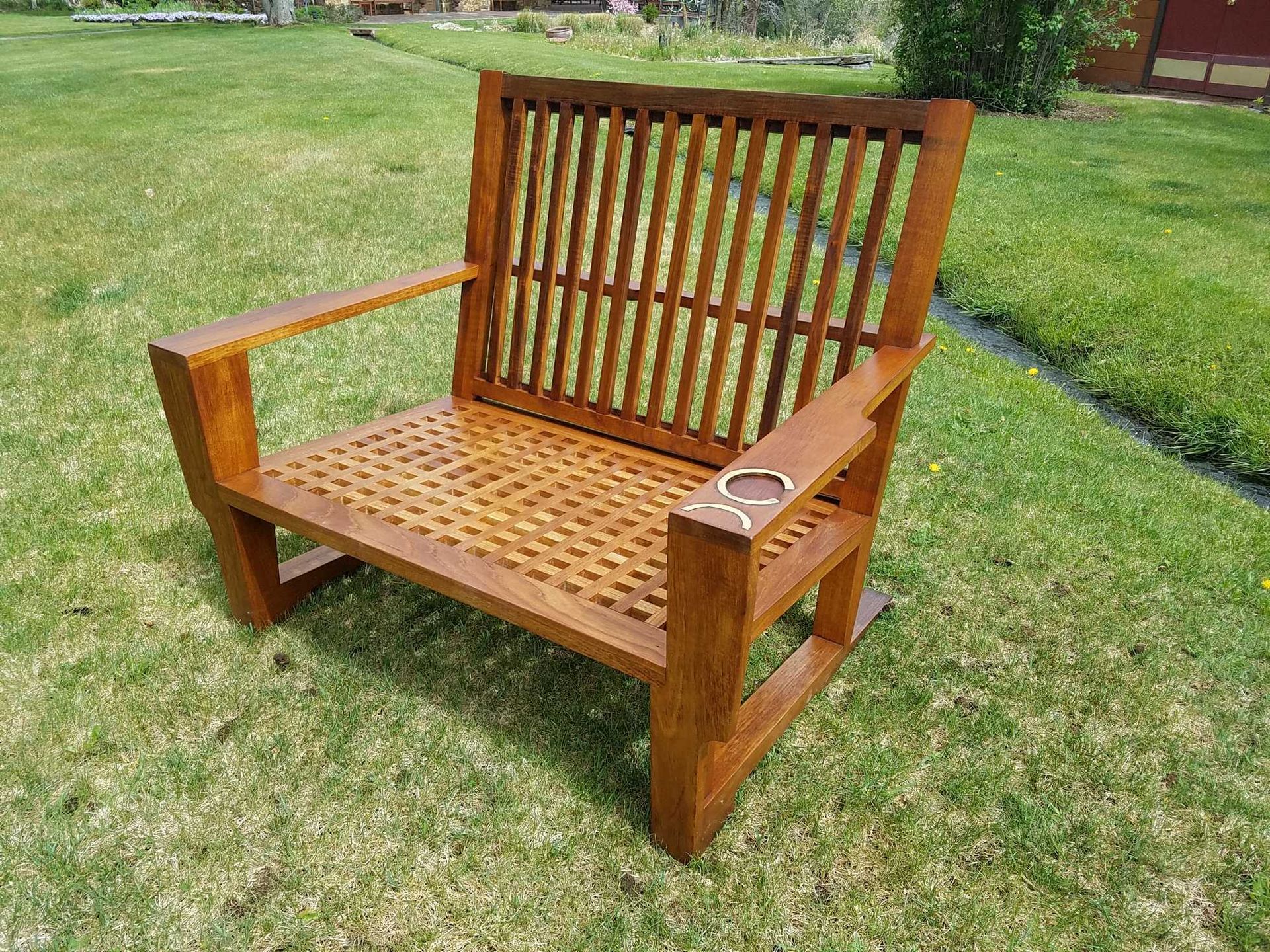 Wooden outdoor chair on grass. Brown chair with slatted back and seat; cup holder on armrest.