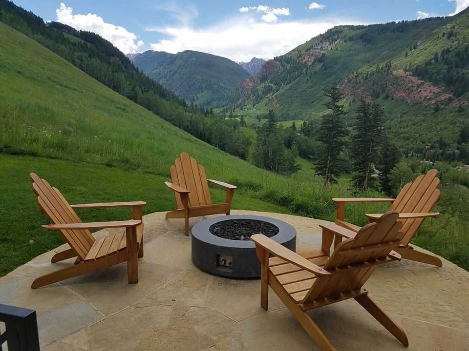 Four wooden Adirondack chairs around a fire pit on a patio, mountains in the background.