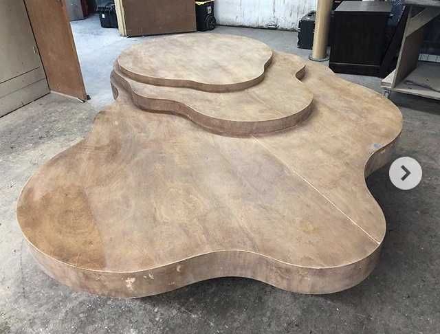 Wooden, cloud-shaped coffee table with three levels, stained brown, in a workshop setting.