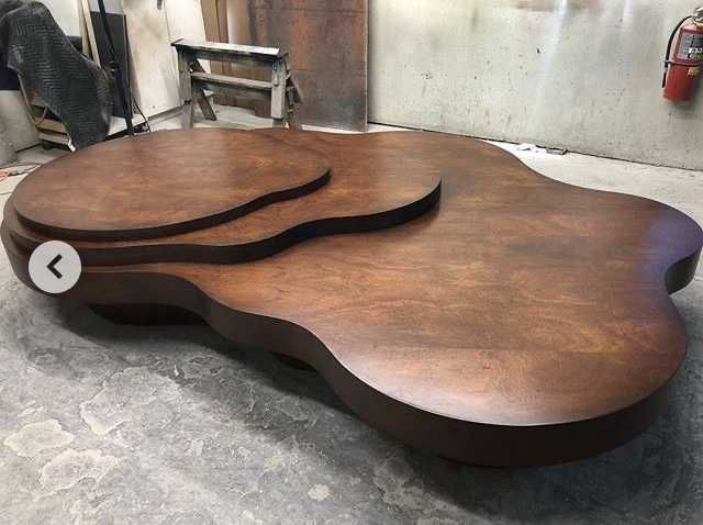 Wooden, irregularly shaped coffee table in a workshop setting, stained dark brown with a tiered surface.